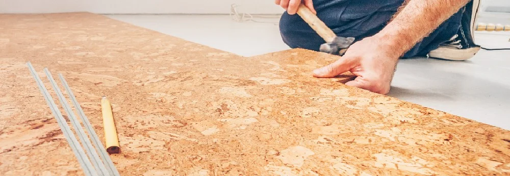 Person verlegt Korkboden mit Hammer